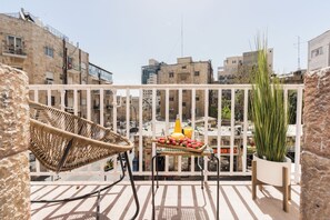 A balcony with a wicker chair, a table with fruits and a bottle, and a potted plant.