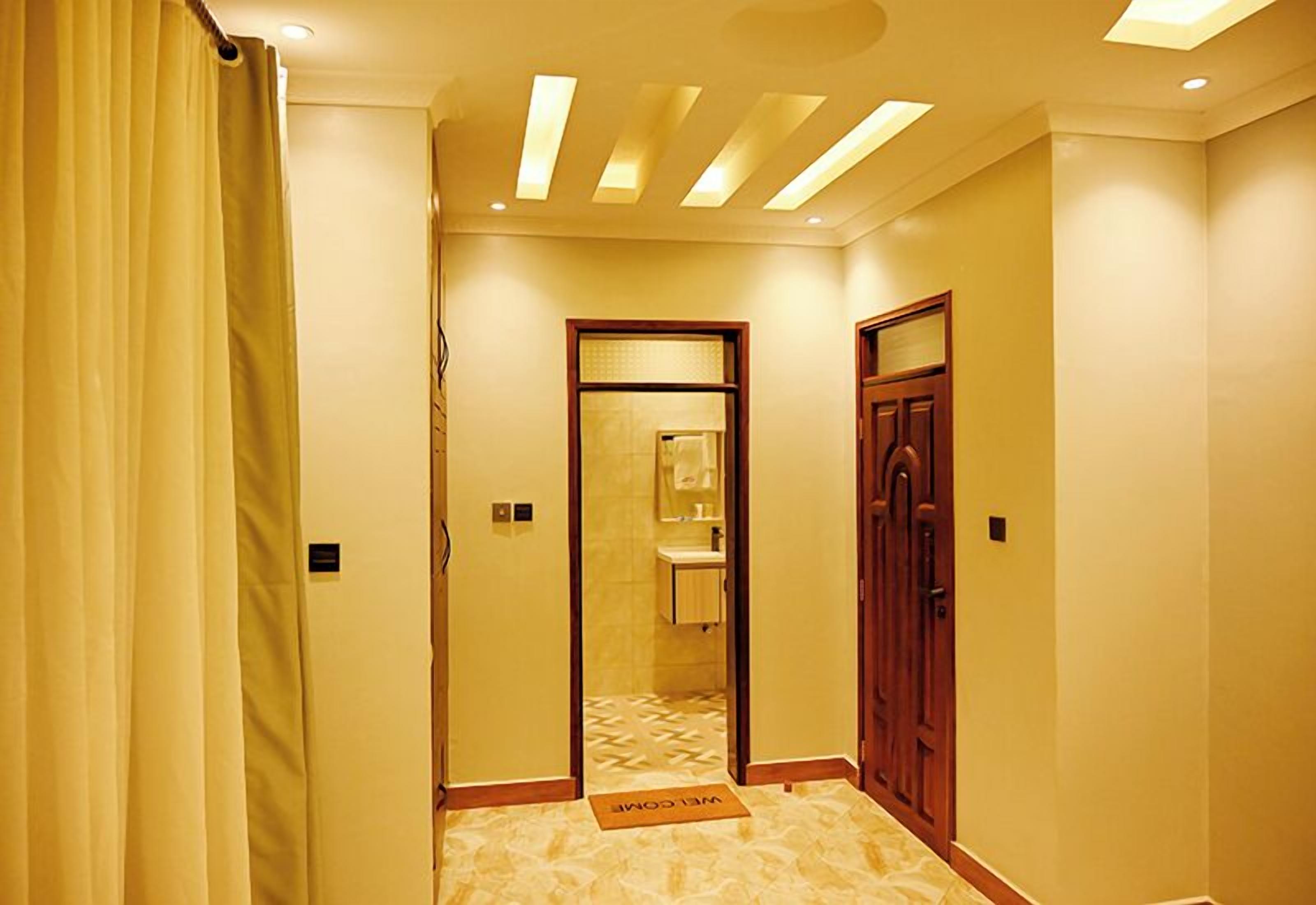 A hotel hallway with a reception desk, a door to a bathroom, and a doormat with "WELCOME" written on it.