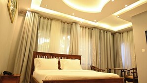 A bedroom with a wooden bed, a nightstand, and a chair. - Neon Hotel Ntinda (Kampala)