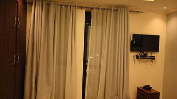 Ein Hotelzimmer mit Bett, Wandfernseher, Holzschrank und beigen Vorhängen.
