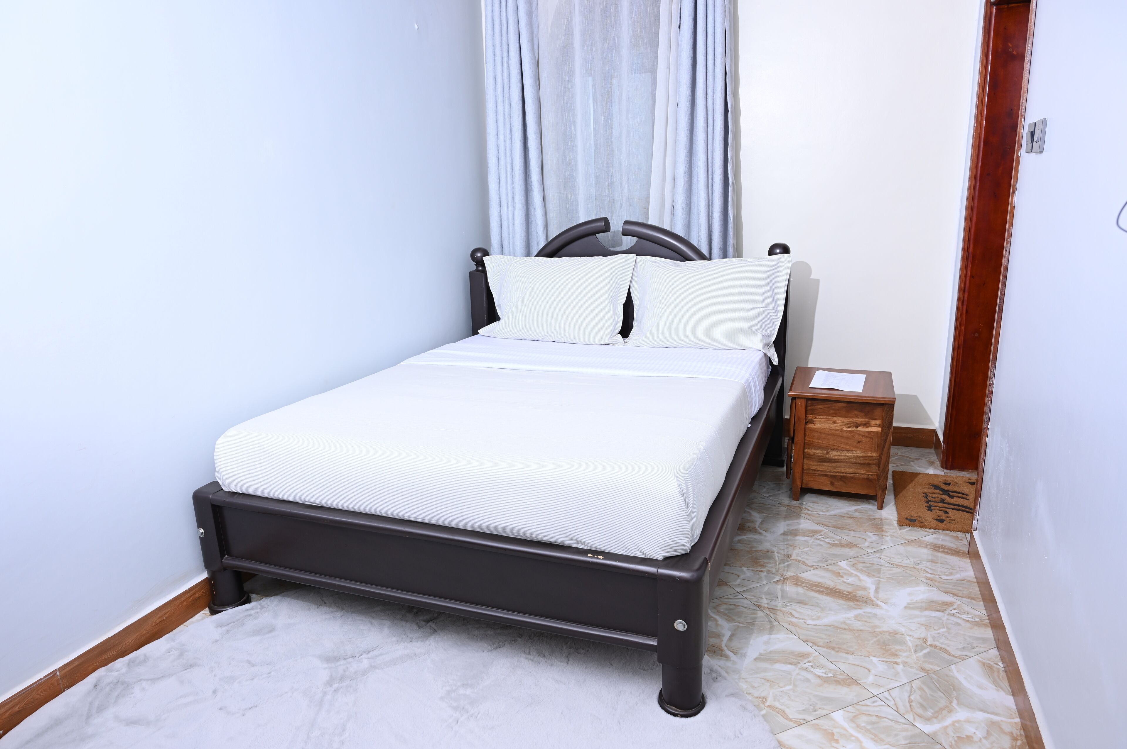 Uma cama com colchão e travesseiros brancos, cabeceira de madeira e uma pequena mesa de cabeceira com uma caixa de lenços.
