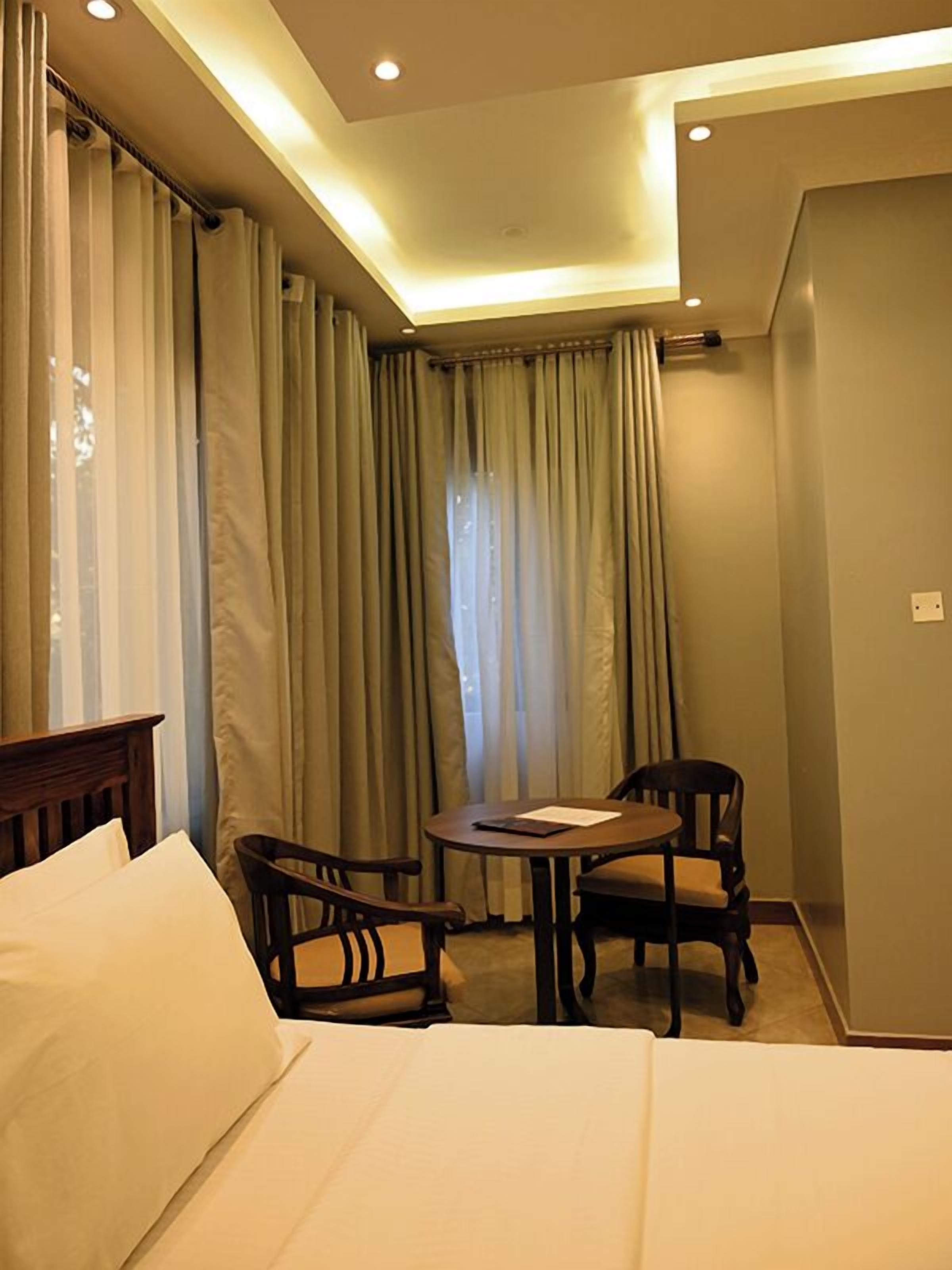 A hotel room with a bed, two chairs, a small table, and a window with curtains.