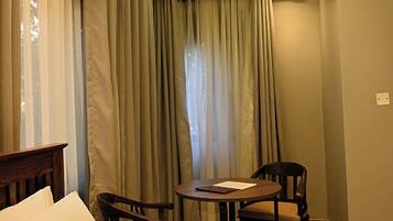 A hotel room with a bed, two chairs, a small table, and a window with curtains.