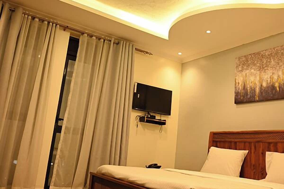 Quarto moderno com cama de madeira, televisão de tela plana fixada na parede e teto com iluminação embutida.
