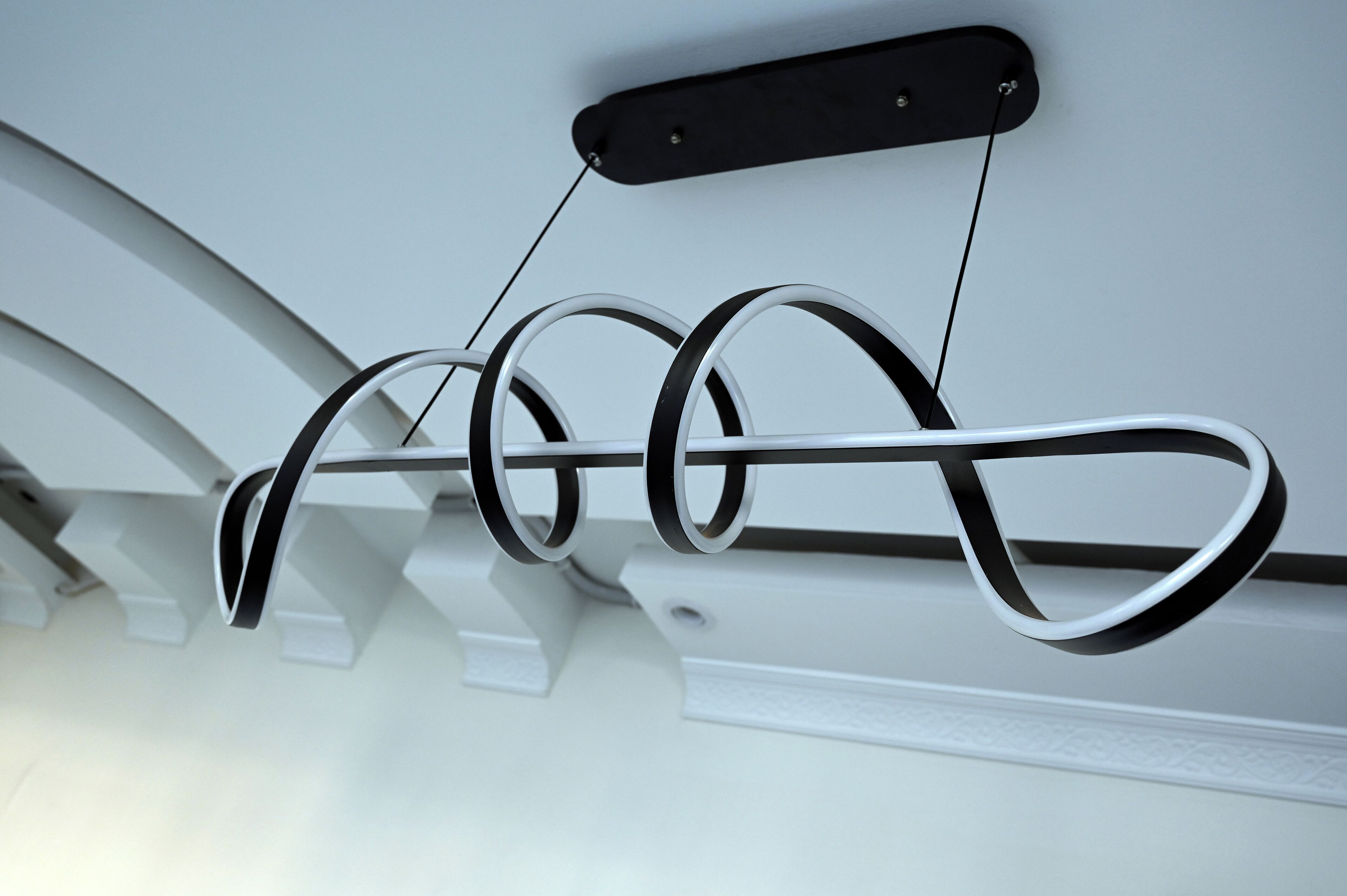 A ceiling-mounted, white, curved, metal structure with a black rectangular element attached to it.