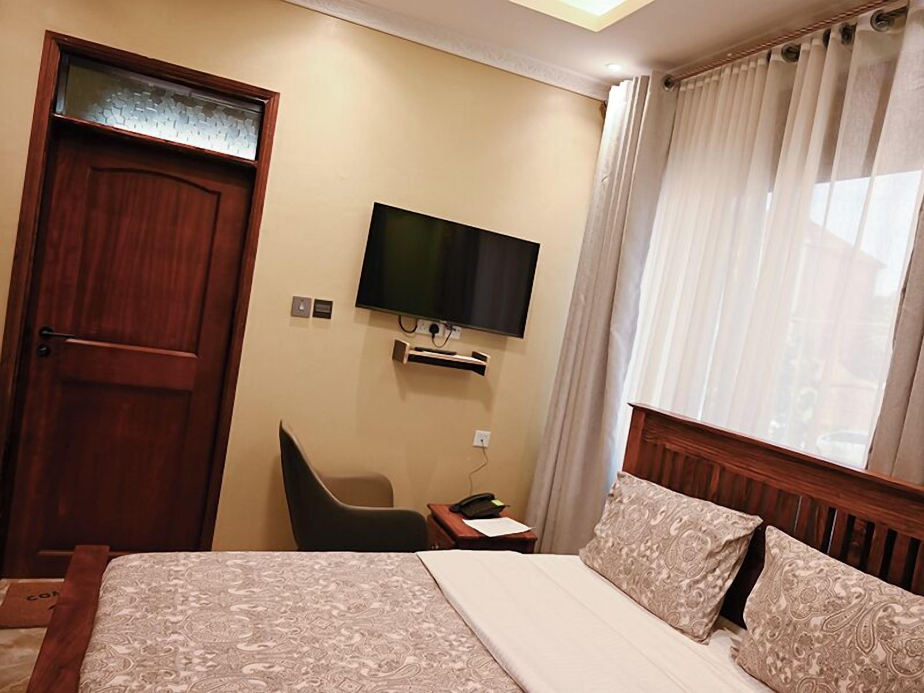 Ein Hotelzimmer mit Bett, Wandfernseher, Schreibtisch mit Stuhl und einem Vorhangfenster.