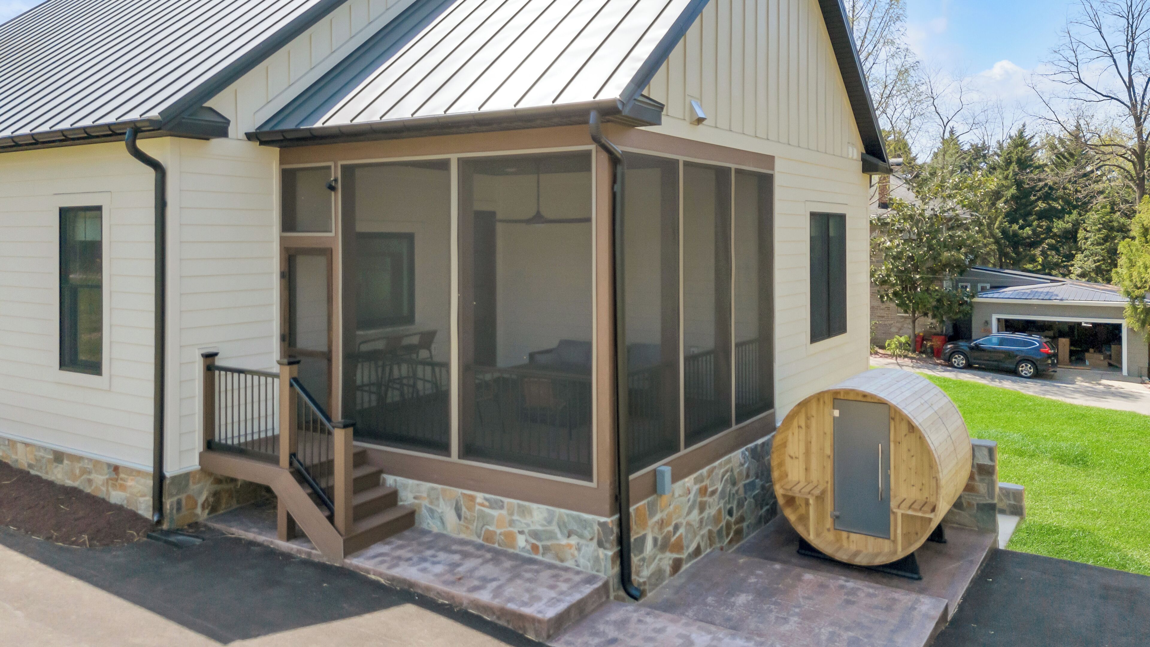 A house with a covered porch, a stone foundation, and a wooden barrel.