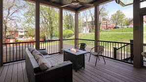 Een overdekt terras buiten met een bank, stoelen en een vuurkorf.