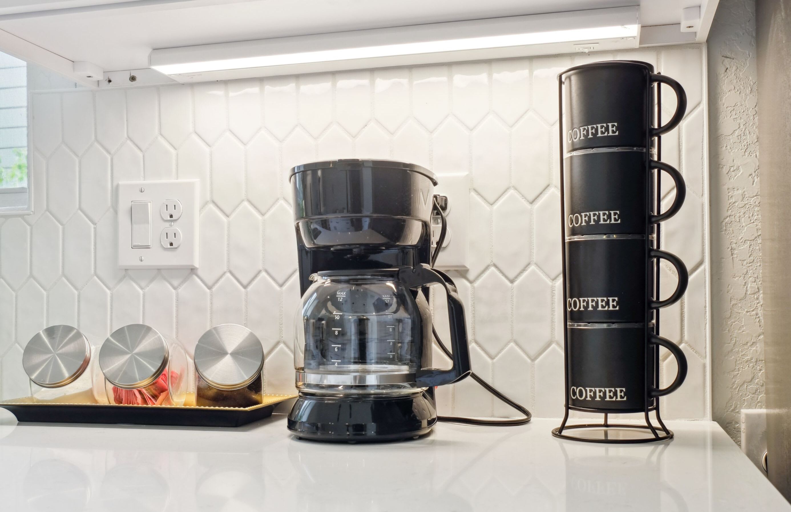 A kitchen with a coffee maker, a tray with three cups, and a coffee mug rack.