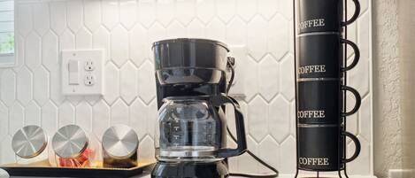 A kitchen with a coffee maker, a tray with three cups, and a coffee mug rack.