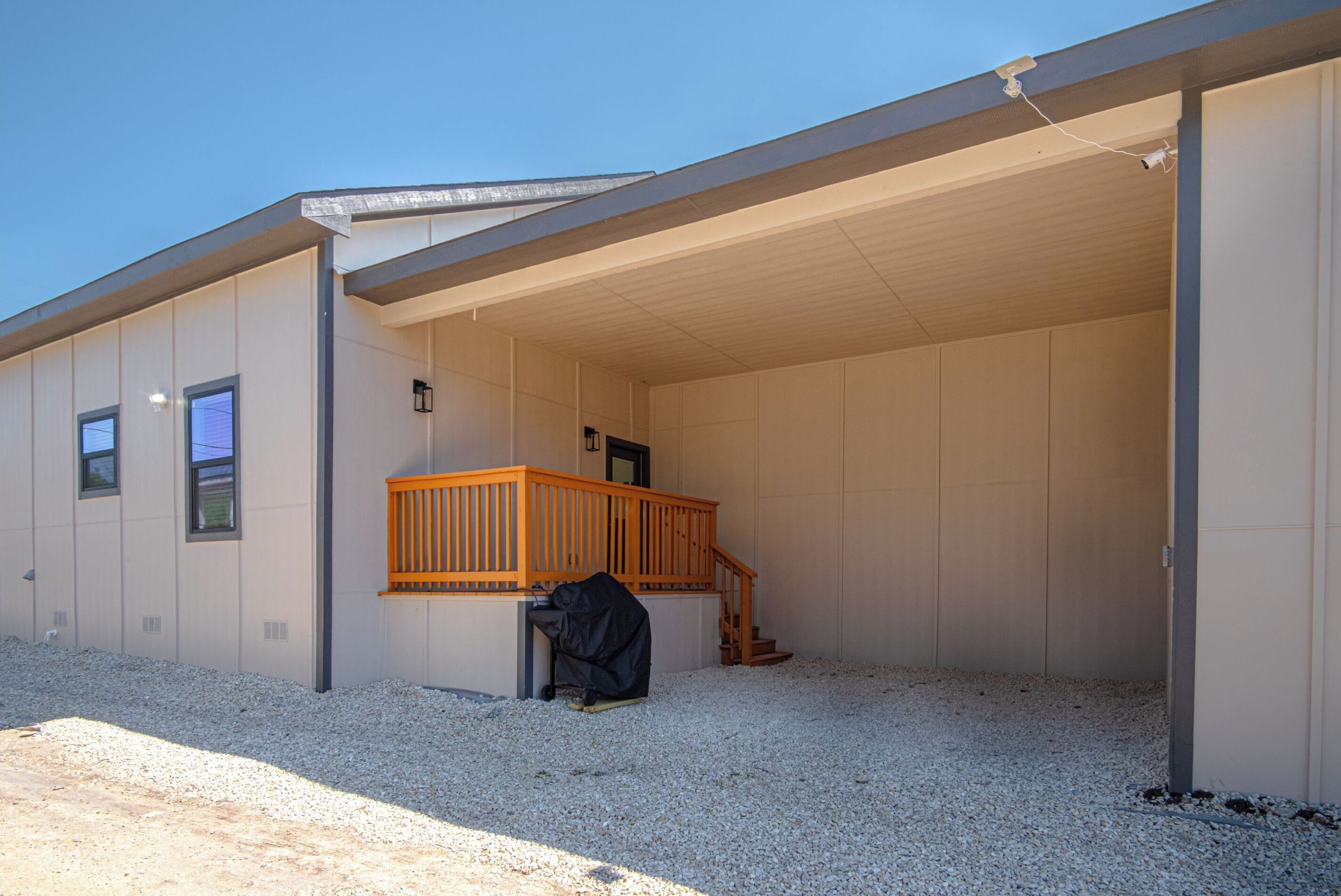 En bygning med et overdækket område, en trætrap og en person, der sidder ned i nærheden af indgangen.