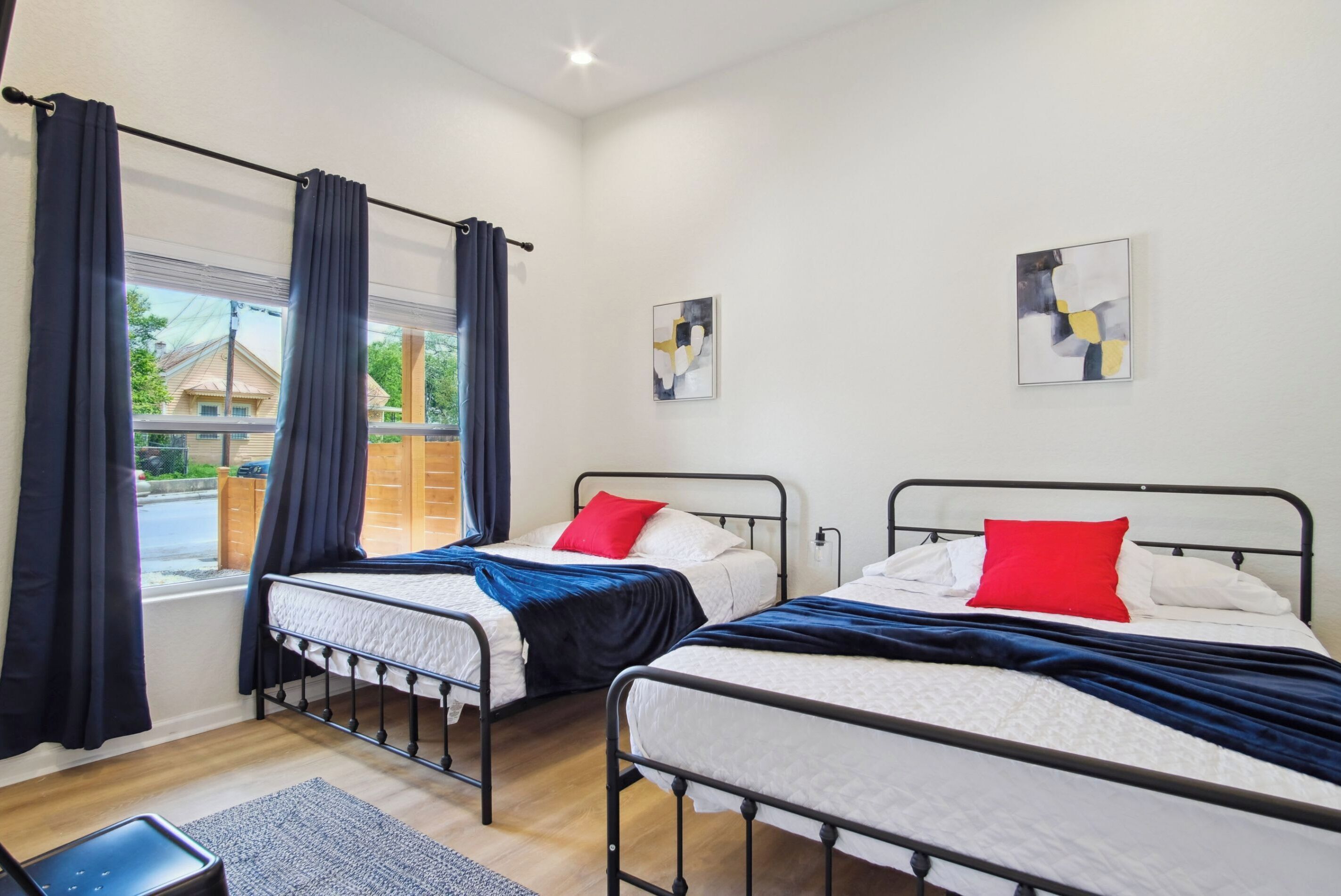 A room with two beds, a window with curtains, and two abstract paintings on the wall.