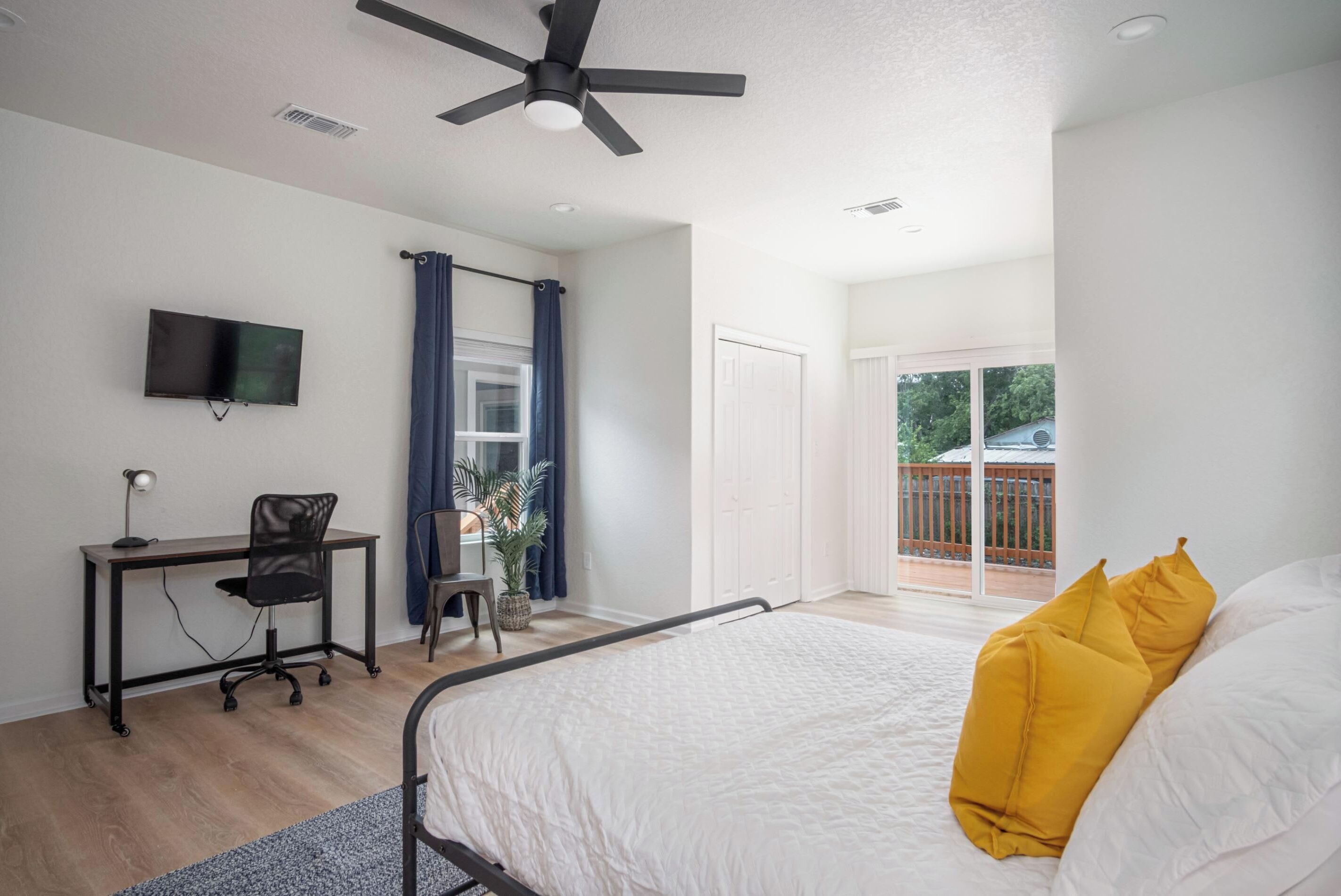A bedroom with a bed, a desk with a chair, a TV, and a balcony with a view.