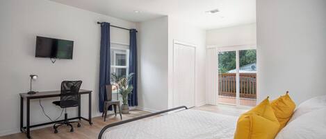 A bedroom with a bed, a desk with a chair, a TV, and a balcony with a view.