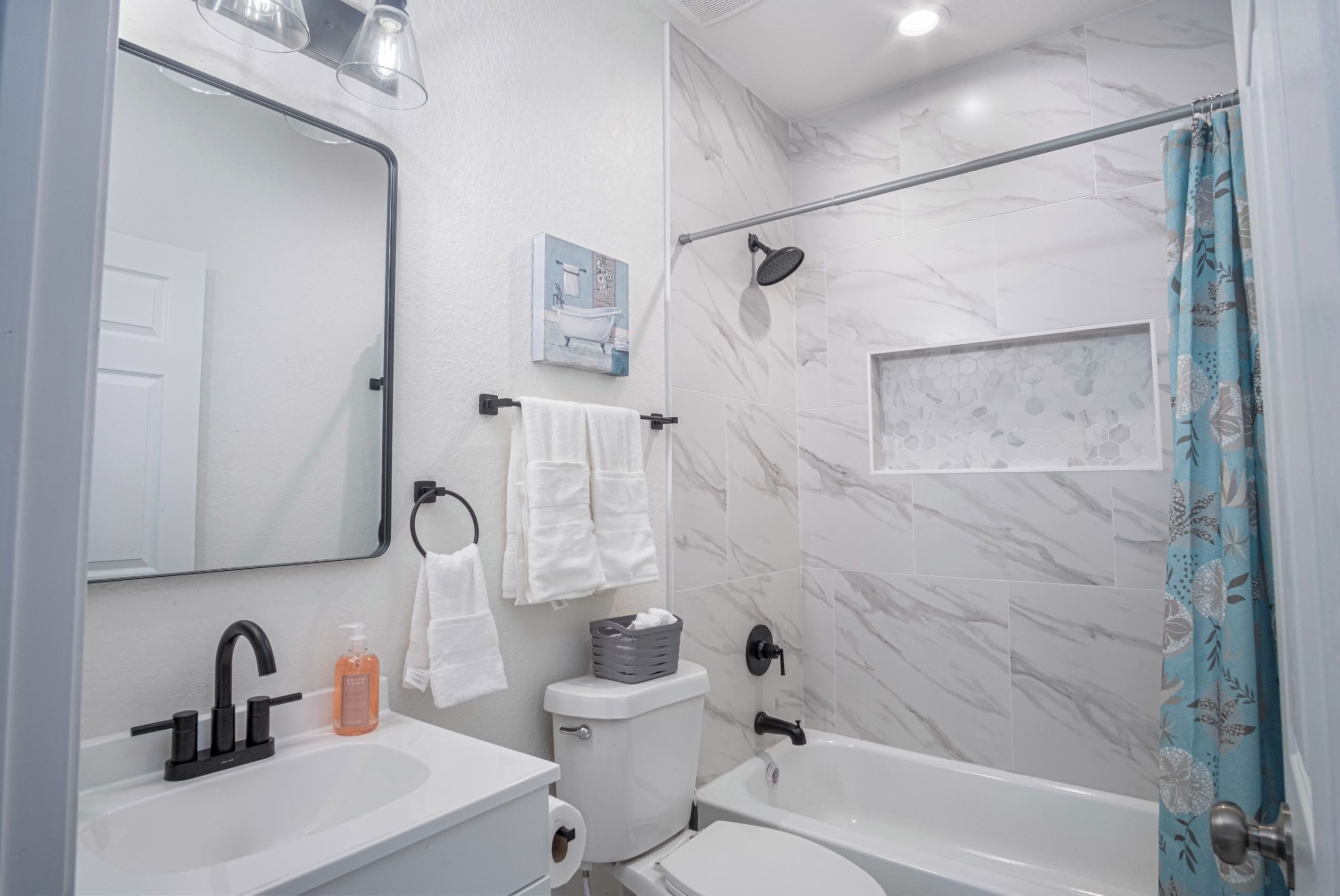 A modern bathroom with a white sink, toilet, and bathtub. There is a shower curtain, a towel rack, and a mirror.
