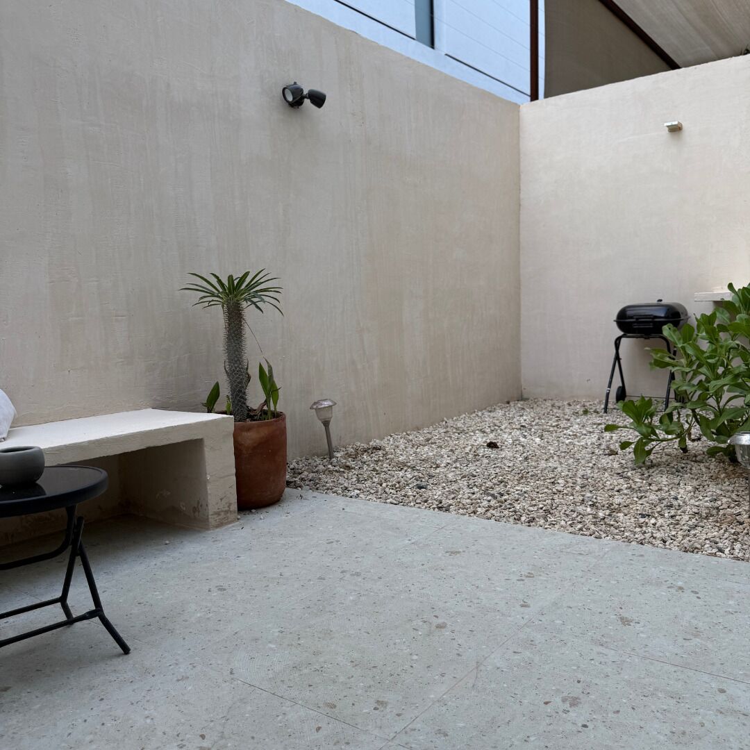 A patio area with a concrete bench, a potted plant, a small table, and a grill.