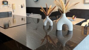 Ett modernt kök med en svart bänkskiva i marmor, två unika vita vaser med torkat pampasgräs och en väggmonterad spegel.