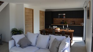 A modern living room with a sofa, a dining table with chairs, and a kitchen area with dark cabinets and wooden accents.