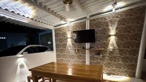 A dining area with a wooden table and benches, a TV mounted on a textured wall, and a car parked outside.