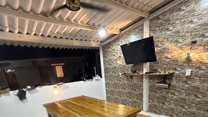A wooden dining table with benches, a TV mounted on the wall, and a stone-textured wall.