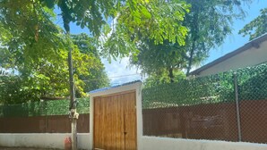 A fenced outdoor area with a wooden gate, surrounded by a white wall and a green fence.