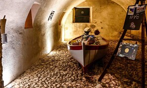 Una stanza rustica con pavimento in pietra, una barca e una piccola finestra.