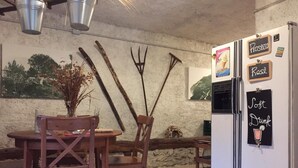 Een landelijke keuken met een houten tafel en stoelen, een koelkast, en decoratieve elementen zoals een drietand en een vaas met gedroogde planten.