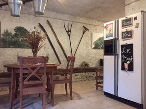 Una cucina rustica con un tavolo e sedie in legno, un frigorifero e oggetti decorativi come un tridente e un vaso con piante secche.