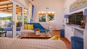 Une pièce confortable avec un canapé, une table basse et un téléviseur. Il y a deux portes qui donnent sur l’extérieur, ainsi qu’une fenêtre avec des rideaux.