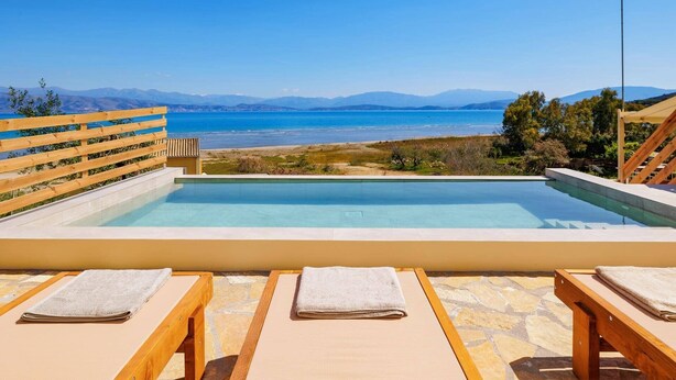 Une piscine avec vue sur la mer et les montagnes, des chaises longues en bois et un drapeau.