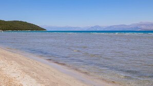 Une plage à l’eau claire, bordée d’un rivage sablonneux, avec des montagnes qui se dessinent à l’horizon.