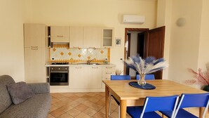 A compact living space with a kitchenette, a dining area with blue chairs, and a gray sofa. - Nala House - Villa 800 mt from the sea (Budoni)