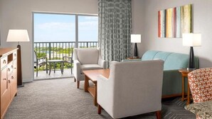 A hotel room with a balcony, a sofa, two armchairs, a TV, and a bed.
