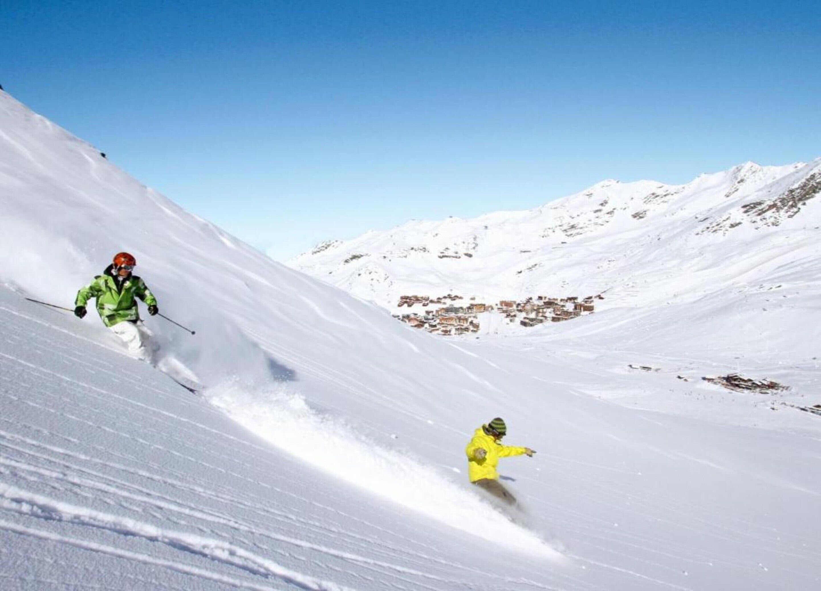 A snowy mountain slope with two skiers.