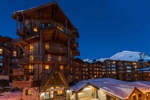A multi-story wooden building with balconies, a stone base, and a snow-covered mountain in the background.