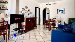 A living room with a television displaying 'NETFLIX', a dining area with chairs and a table, and a sofa. - Aeolian Villa - Apartment with two bedrooms, sea view, and garden (Lipari)