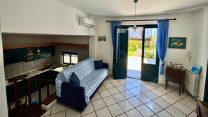 A compact living space with a kitchenette, a sofa, a dining area, and a door leading to a garden. - Aeolian Villa - Apartment with two bedrooms, sea view, and garden (Lipari)