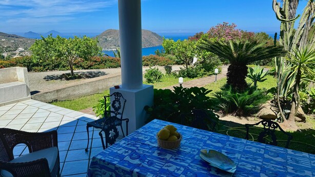A covered patio with a table set for two, overlooking a scenic landscape with mountains and a body of water. - Aeolian Villa - Apartment with two bedrooms, sea view, and garden (Lipari)
