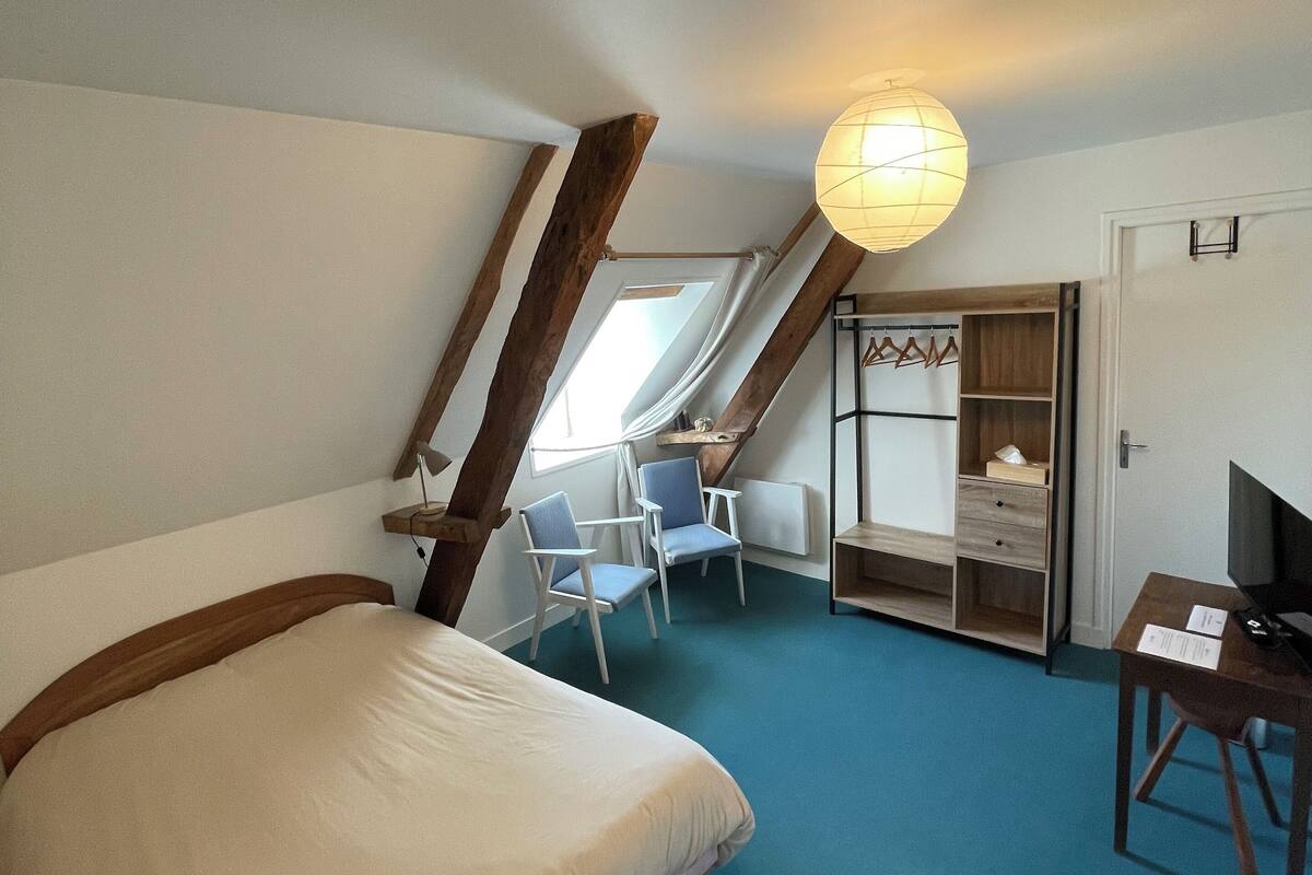 Un dormitorio con una cama grande, un escritorio, dos sillas, un armario y una lámpara en el techo.