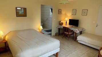 Un dormitorio con dos camas, un escritorio con televisor y un baño visible a través de una puerta abierta.