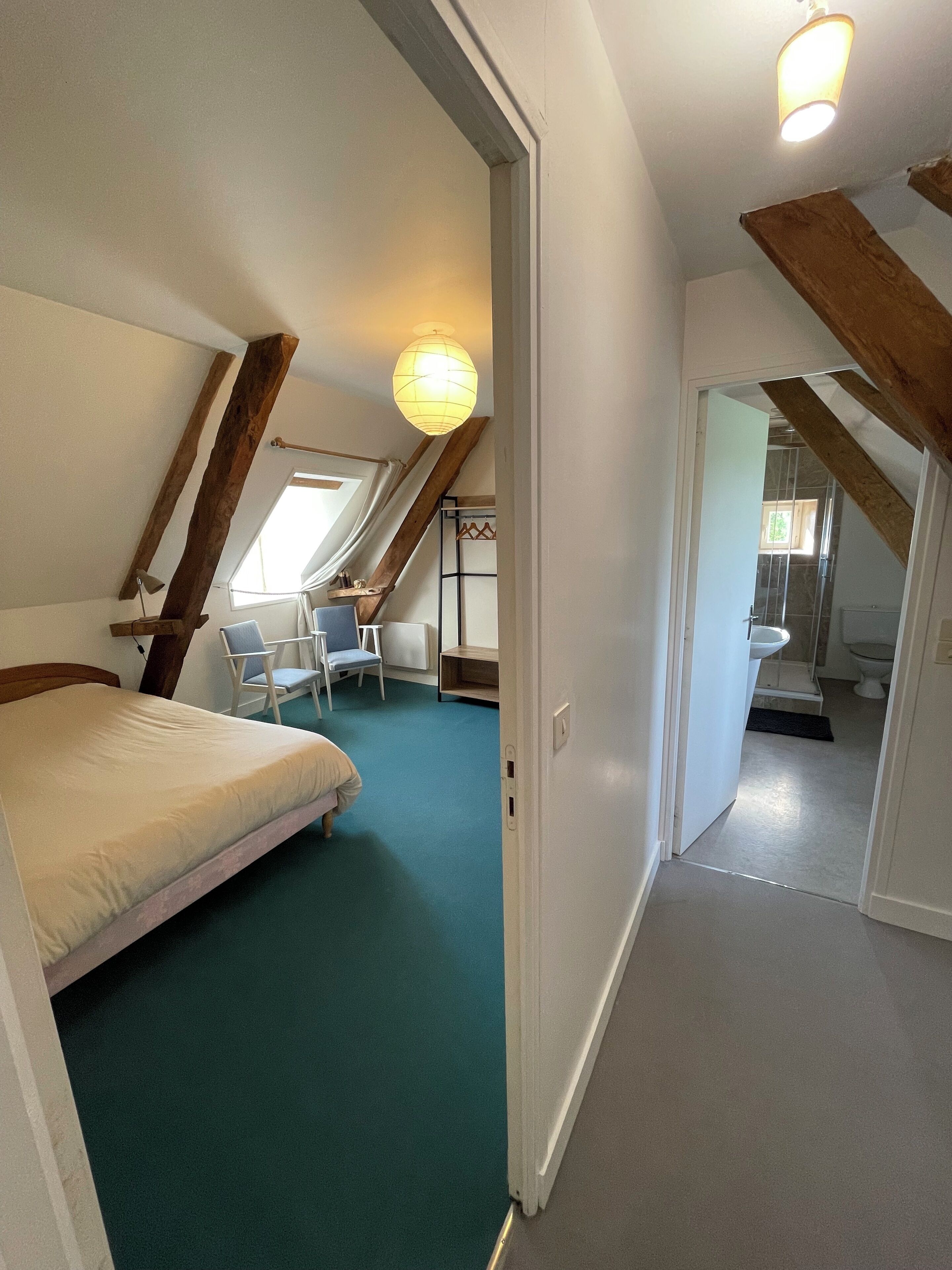 Een slaapkamer met een bed, een stoel en een bureau. Er is een raam en een deur naar een badkamer.