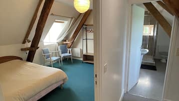 Een slaapkamer met een bed, een stoel en een bureau. Er is een raam en een deur naar een badkamer.