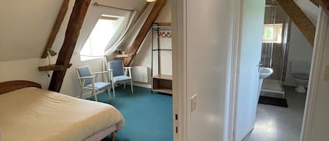 Een slaapkamer met een bed, een stoel en een bureau. Er is een raam en een deur naar een badkamer.
