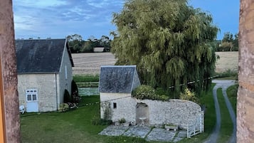 A rural landscape with stone buildings, a tree-lined path, and a clear sky.