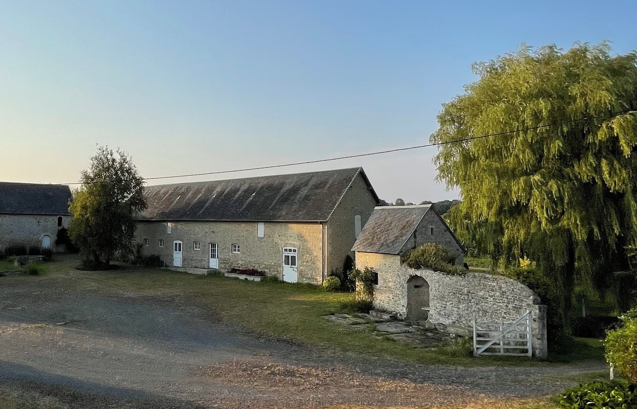 A stone building with a sloped roof, a small attached structure, and a gate.