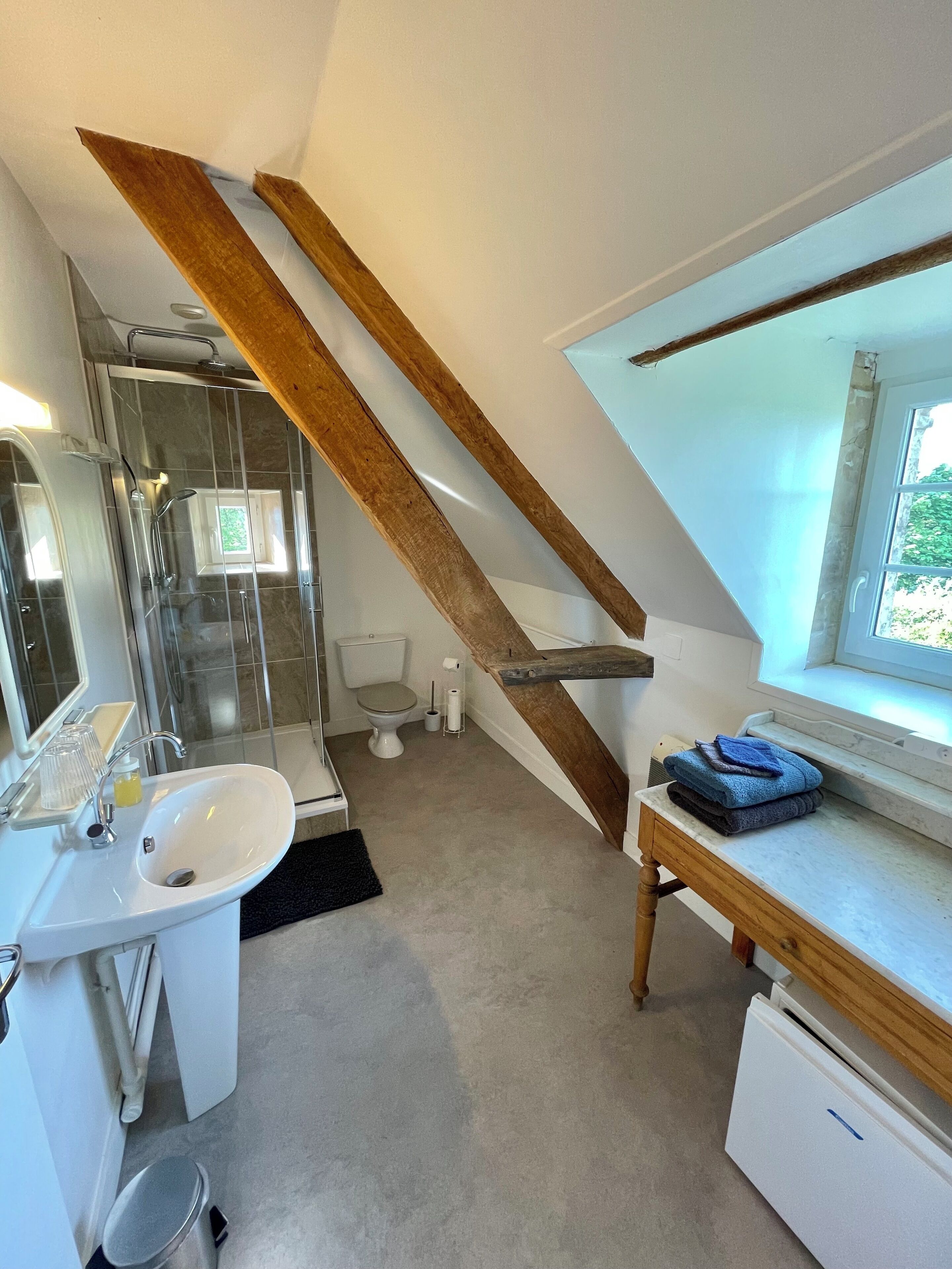 A modern bathroom with a shower, toilet, and sink. A wooden staircase leads to a loft area with a window.