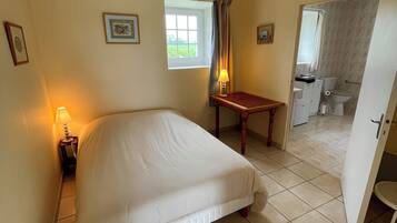Un dormitorio con cama, lámpara de noche, ventana y vista al baño.