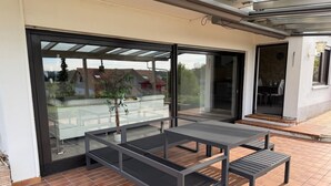 Eine moderne Terrassengruppe im Freien mit Glastisch und Bänken, einem Blumentopf und Blick auf die Nachbarschaft.