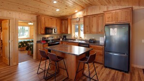 Cocina de cabaña de madera con una isla central, taburetes de bar, un refrigerador y una ventana.