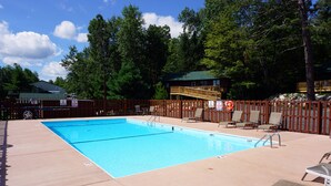 Una piscina rectangular con muelle de madera, rodeada por una cerca también de madera, y un pequeño solárium con sillas.